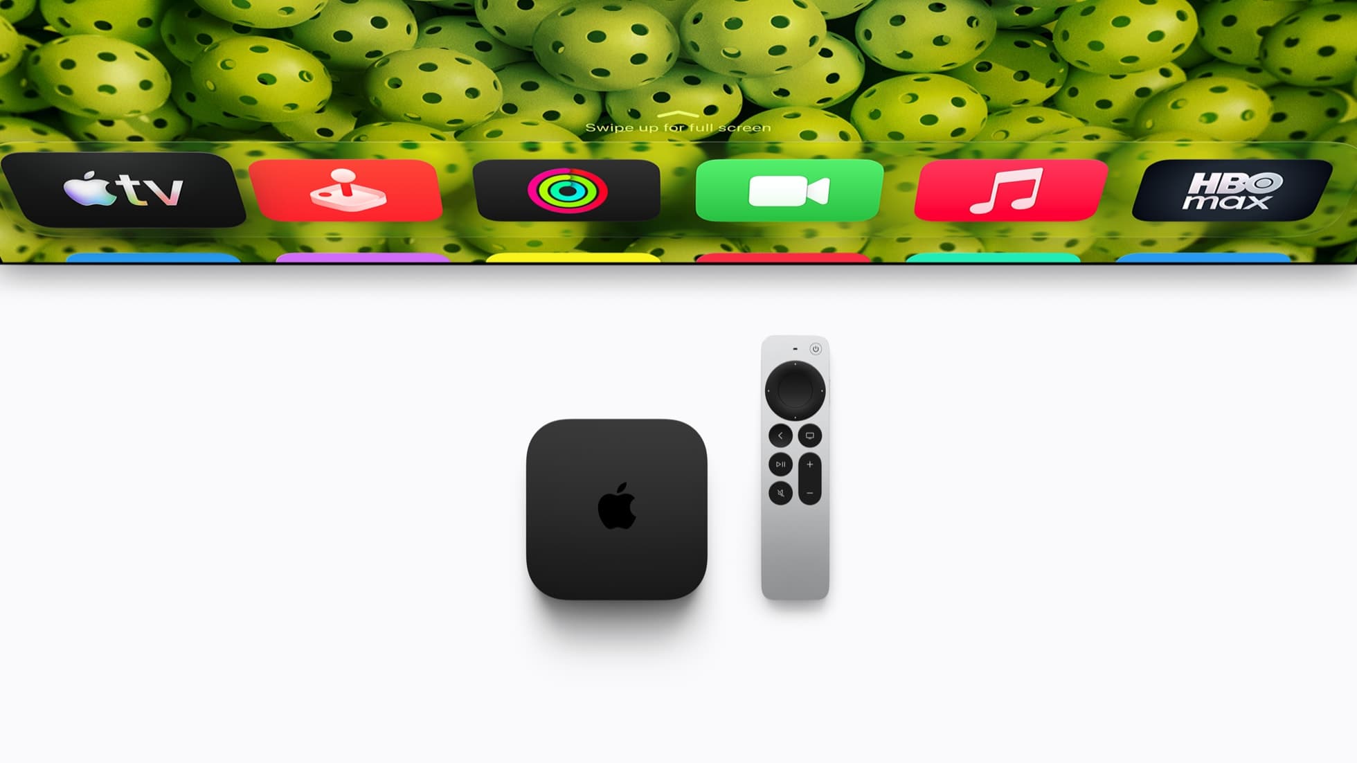 A black Apple TV 4K box with a silver Apple logo sits beside an upright silver Siri Remote on a white surface, below the bottom edge of a television screen showing a row of app icons over a wallpaper of green pickleballs.