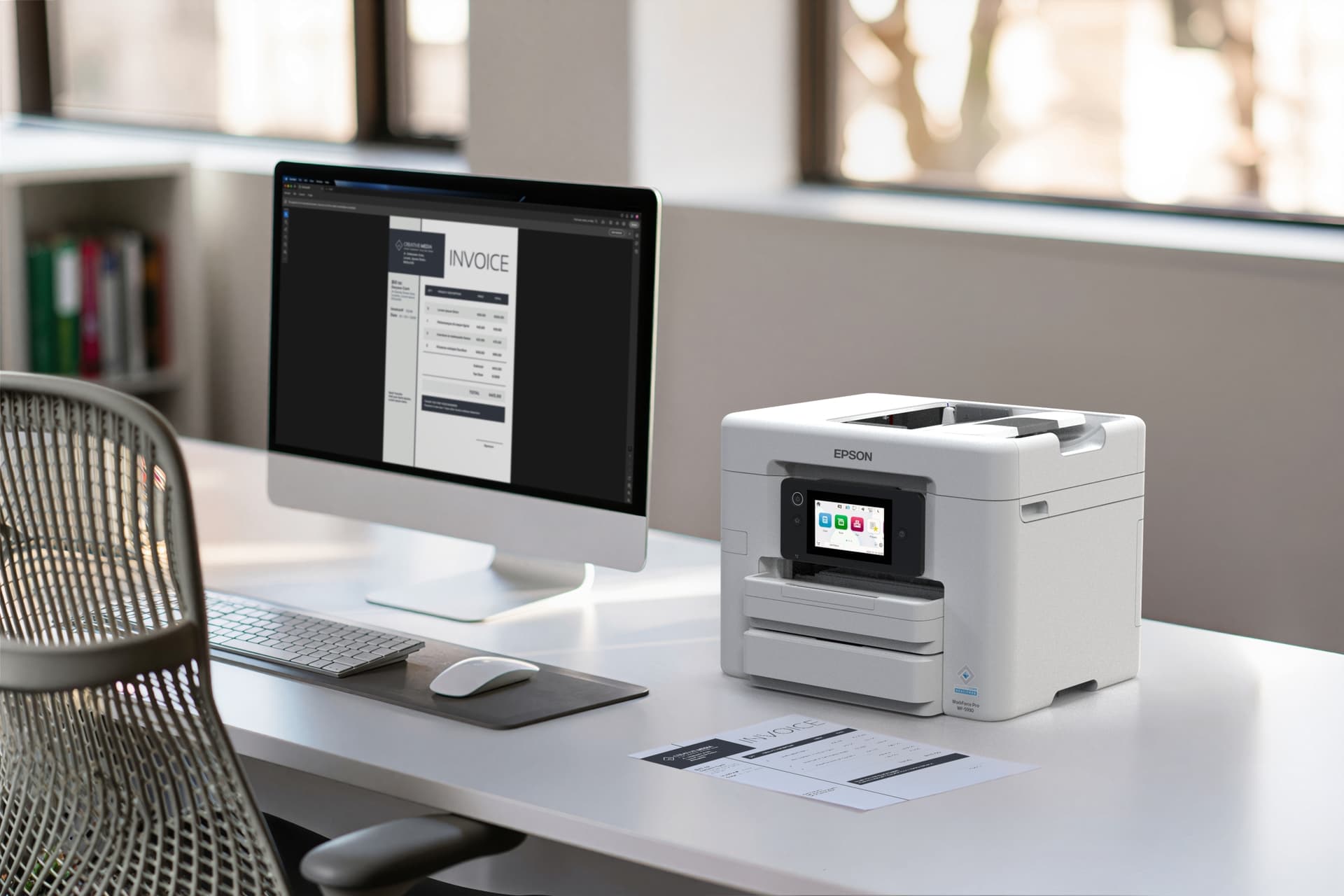 A white Epson WorkForce Pro WF-5930 printer with a small color touchscreen and two paper trays sits on a white desk beside a silver all-in-one computer showing an invoice, with a keyboard and a white mouse in front of it; a printed copy of the invoice lies on the desk and a mesh office chair is in the foreground.
