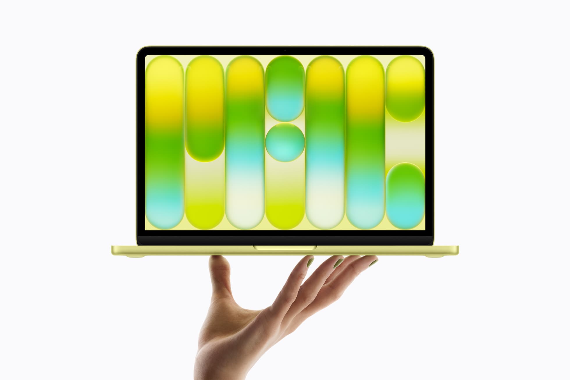 A citrus-yellow MacBook Neo held open on the fingertips of an upturned hand against a white background, its screen filled with a wallpaper of vertical yellow, green and aqua capsule shapes; the nails on the hand are painted green to match.